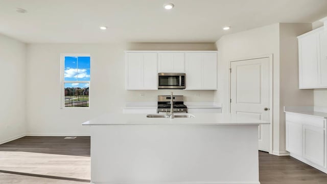 kitchen with an island with sink, white cabinetry, appliances with stainless steel finishes, light countertops, and dark wood-style flooring