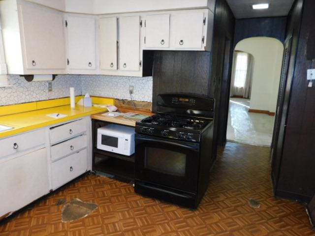 kitchen with white microwave, arched walkways, light countertops, white cabinets, and black range with gas cooktop