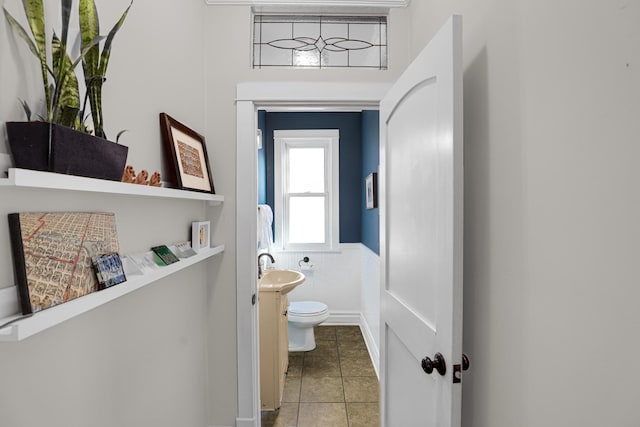 bathroom featuring tile patterned flooring, toilet, a wainscoted wall, and a sink