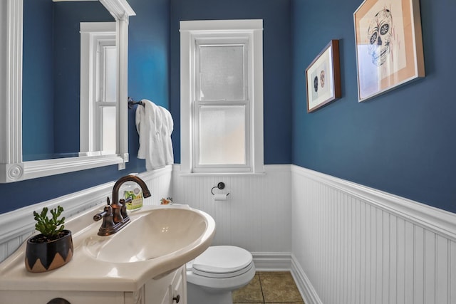 bathroom featuring a wainscoted wall, toilet, vanity, and tile patterned flooring