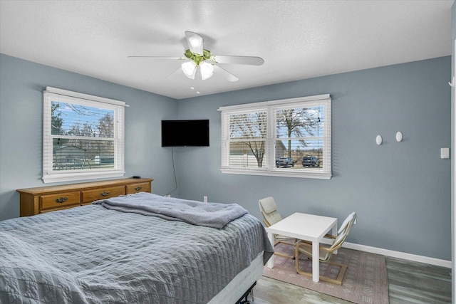 bedroom featuring a ceiling fan, a textured ceiling, baseboards, and wood finished floors