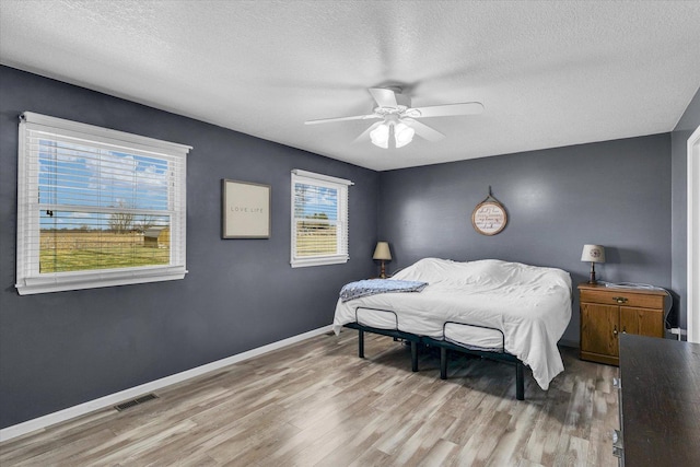 bedroom featuring light wood-style flooring, a textured ceiling, baseboards, and visible vents