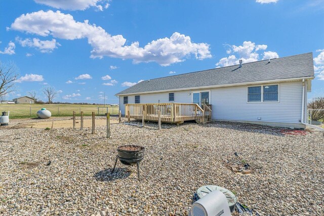 rear view of property featuring an outdoor fire pit, roof with shingles, fence, and a deck