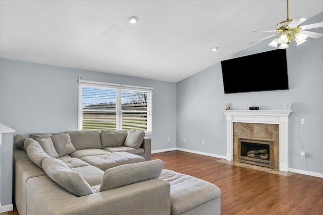living area with vaulted ceiling, a ceiling fan, a fireplace, wood finished floors, and baseboards