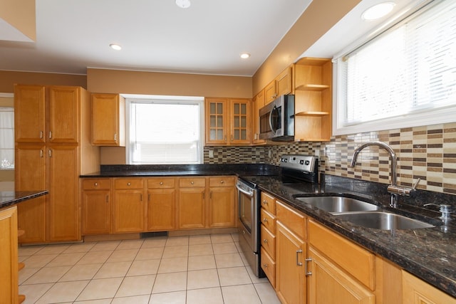 kitchen with a sink, backsplash, stainless steel appliances, brown cabinetry, and light tile patterned floors