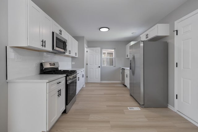 kitchen featuring light wood-style flooring, white cabinetry, stainless steel appliances, light countertops, and decorative backsplash