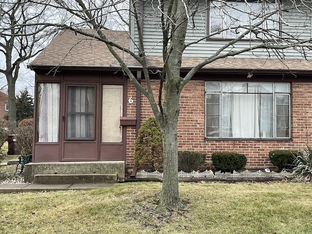 view of front of home featuring entry steps, a front lawn, brick siding, and roof with shingles