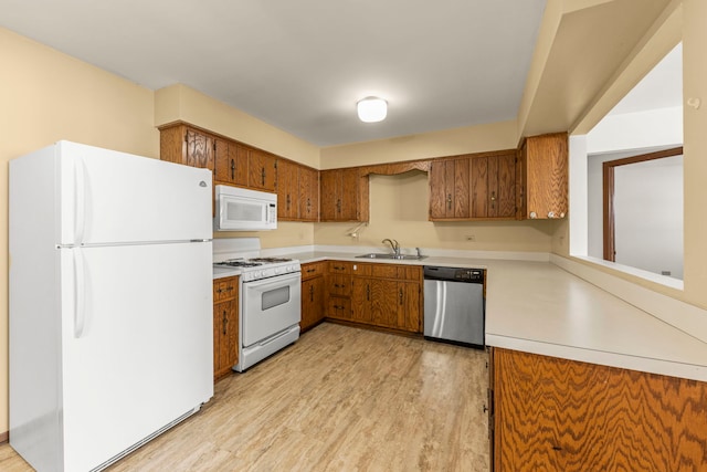 kitchen with light wood finished floors, light countertops, brown cabinets, white appliances, and a sink