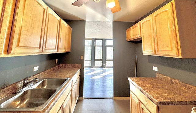 kitchen featuring a ceiling fan, light brown cabinets, baseboards, a sink, and a textured ceiling