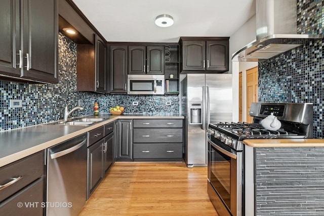 kitchen with light wood finished floors, tasteful backsplash, wall chimney range hood, appliances with stainless steel finishes, and a sink