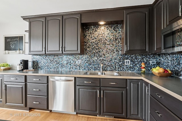 kitchen featuring light wood-type flooring, tasteful backsplash, appliances with stainless steel finishes, and a sink