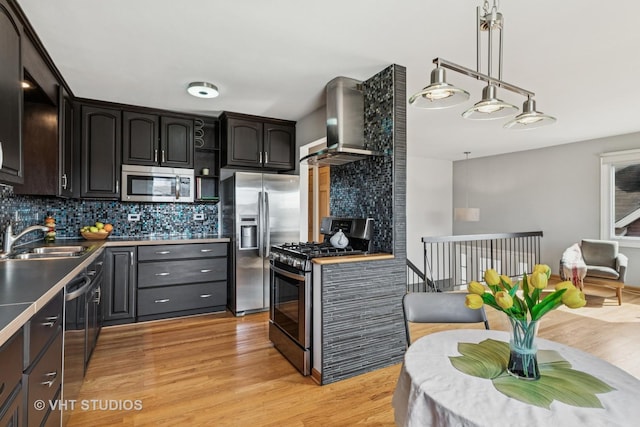 kitchen with wall chimney range hood, light wood-type flooring, decorative backsplash, stainless steel appliances, and a sink