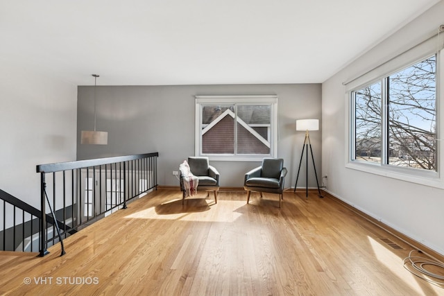 living area with an upstairs landing, visible vents, baseboards, and wood finished floors