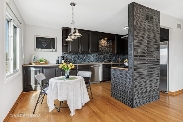 kitchen featuring light wood-type flooring, pendant lighting, tasteful backsplash, stainless steel appliances, and dark cabinets