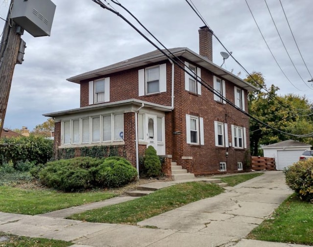 view of front of house with brick siding, a detached garage, a chimney, and an outbuilding