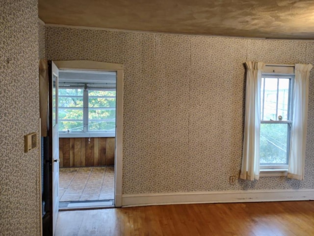 unfurnished room featuring baseboards, wood finished floors, and wallpapered walls