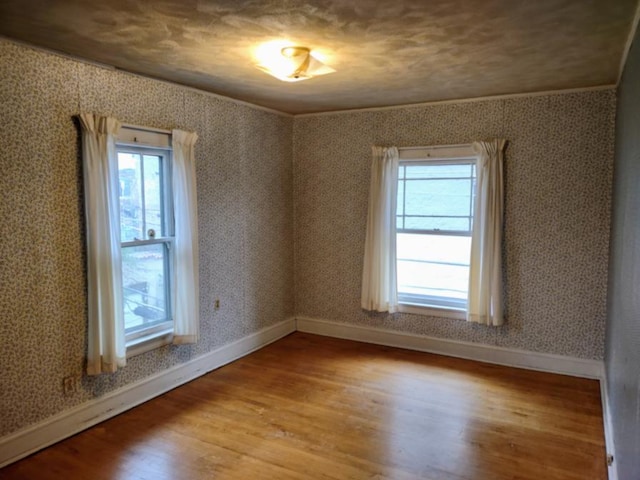 unfurnished room with wallpapered walls, wood finished floors, baseboards, and a healthy amount of sunlight