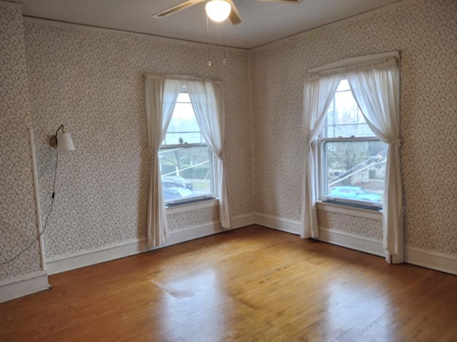 spare room with wood finished floors, baseboards, a ceiling fan, wallpapered walls, and ornamental molding