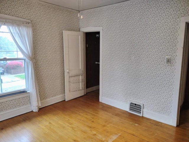 empty room with visible vents, light wood finished floors, baseboards, and wallpapered walls