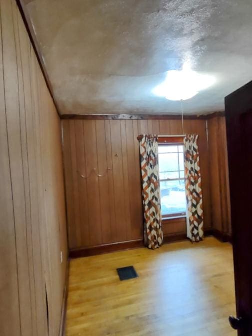 spare room with wooden walls, light wood-style floors, visible vents, and baseboards