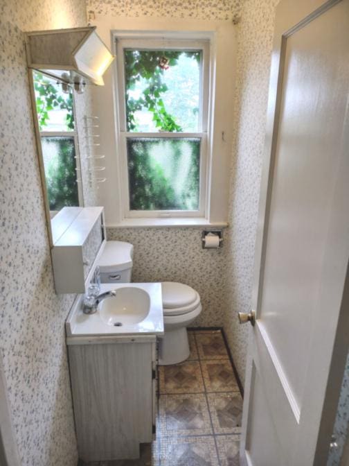 half bath featuring vanity, toilet, and wallpapered walls