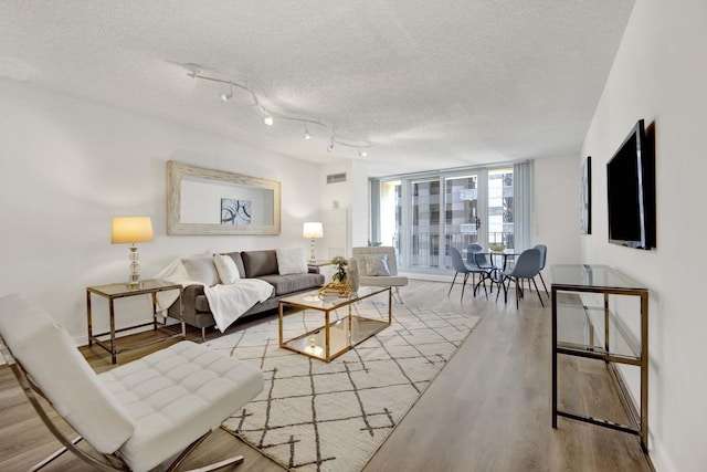 living area with visible vents, expansive windows, a textured ceiling, wood finished floors, and baseboards