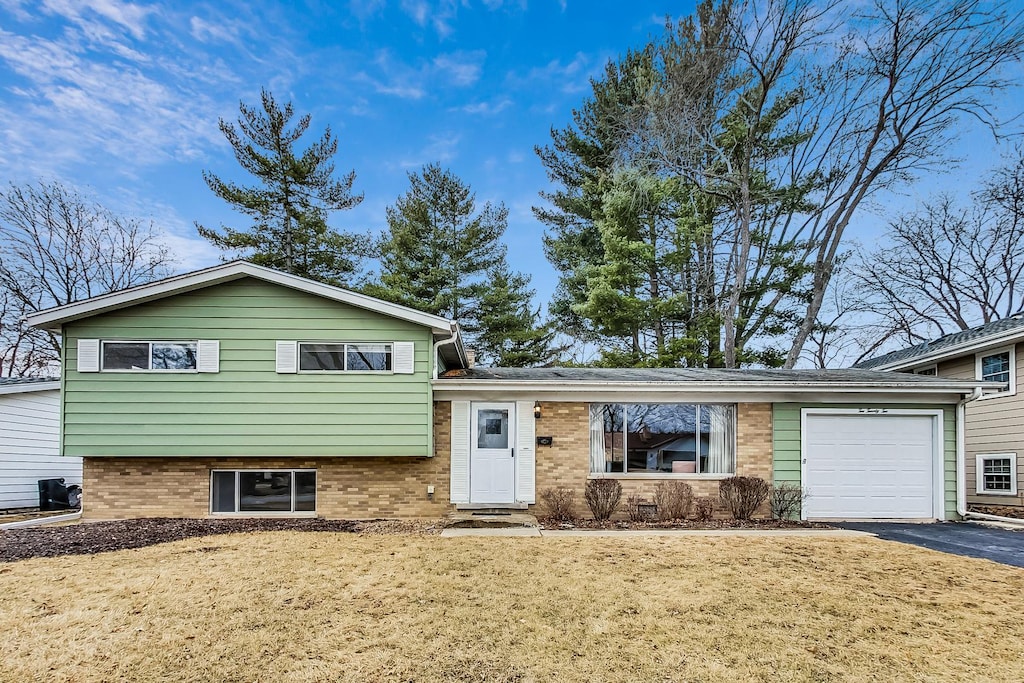tri-level home with brick siding, aphalt driveway, a front yard, and an attached garage