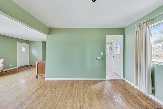 empty room with baseboards, plenty of natural light, and light wood-style flooring