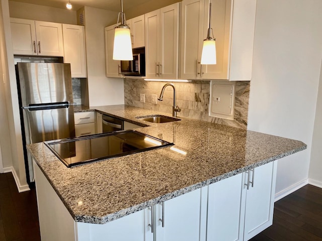 kitchen featuring light stone countertops, a peninsula, stainless steel appliances, a sink, and white cabinets