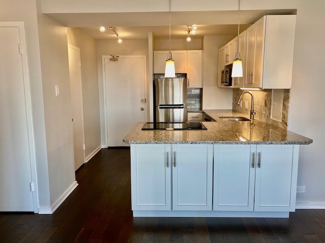 kitchen featuring light stone counters, a peninsula, a sink, appliances with stainless steel finishes, and white cabinetry