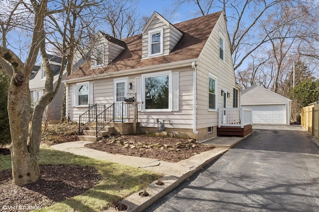 new england style home featuring a garage, roof with shingles, and an outdoor structure