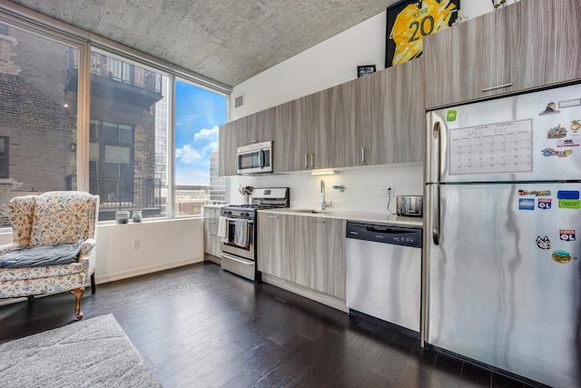 kitchen with dark wood-type flooring, modern cabinets, a sink, appliances with stainless steel finishes, and light countertops