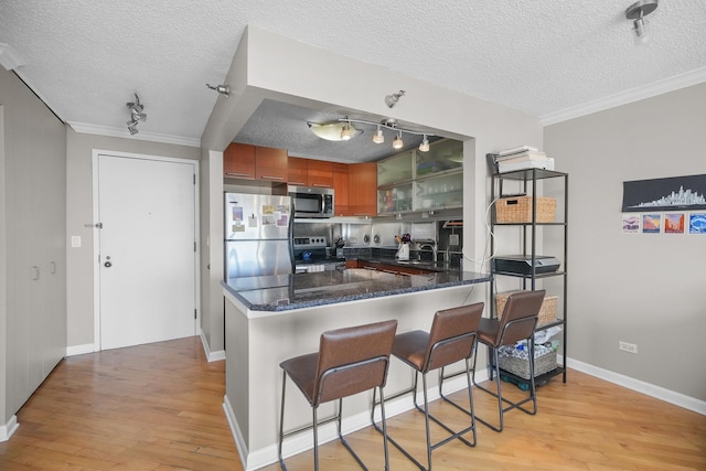 kitchen featuring a peninsula, light wood finished floors, brown cabinets, and appliances with stainless steel finishes