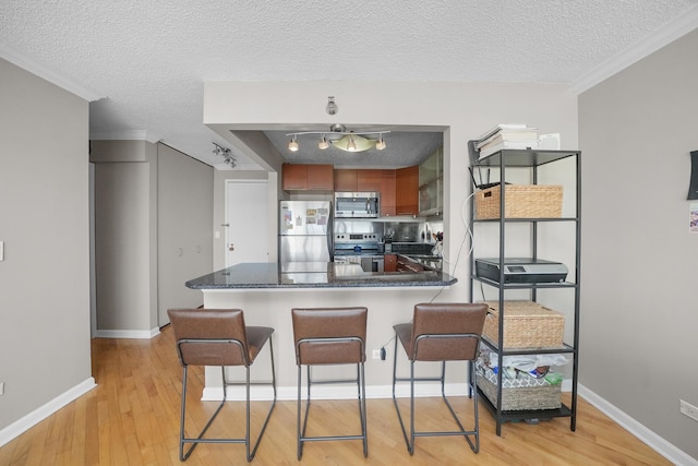 kitchen with light wood-style floors, appliances with stainless steel finishes, a breakfast bar area, a peninsula, and baseboards