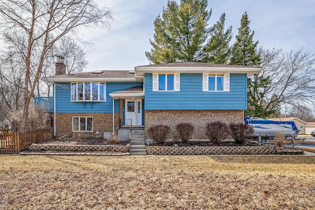 bi-level home with fence, brick siding, and a chimney