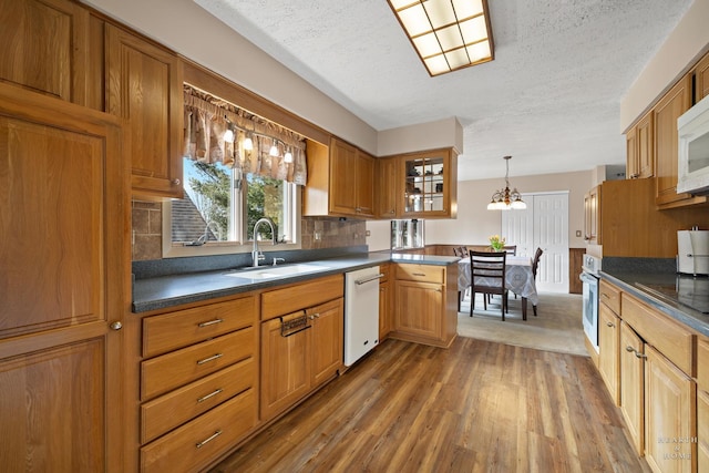 kitchen featuring dark countertops, backsplash, wood finished floors, white appliances, and a sink