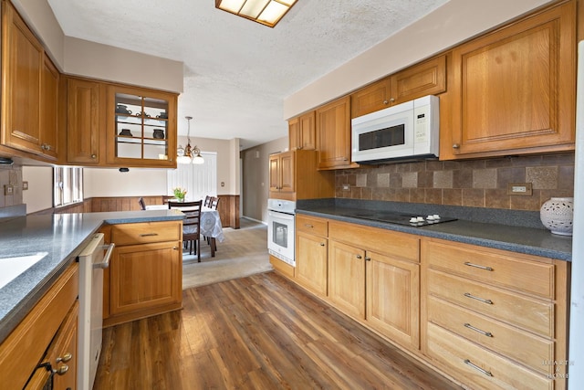 kitchen featuring dark wood finished floors, white appliances, dark countertops, and backsplash