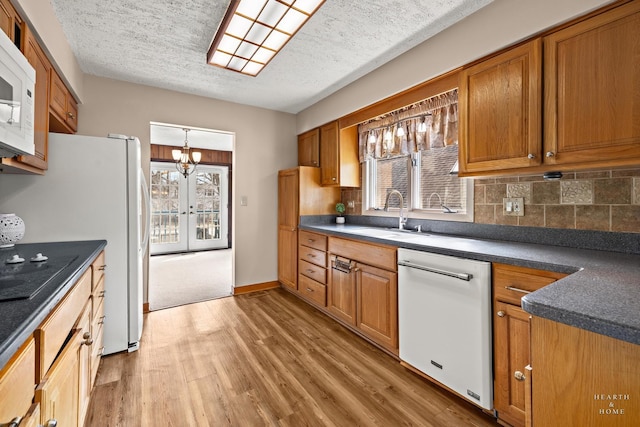 kitchen with light wood-type flooring, a sink, dark countertops, white appliances, and brown cabinetry