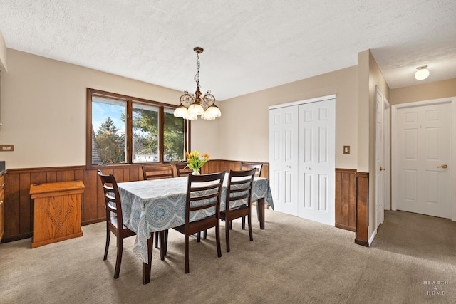 dining space featuring a wainscoted wall, wood walls, a textured ceiling, light colored carpet, and a chandelier