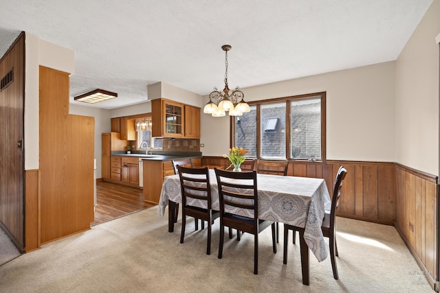 dining room featuring an inviting chandelier, light carpet, wooden walls, and wainscoting