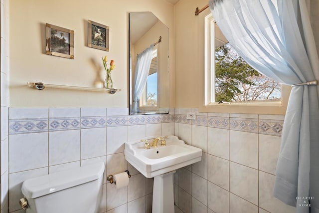 bathroom featuring a wainscoted wall, toilet, tile walls, and a sink