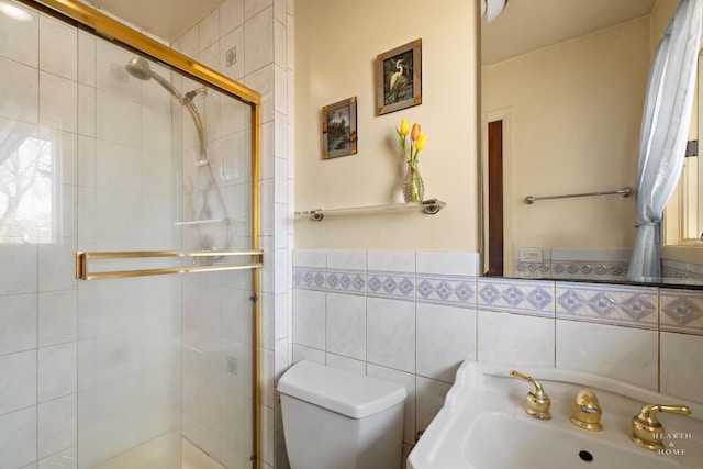 bathroom with a wainscoted wall, toilet, a stall shower, a sink, and tile walls