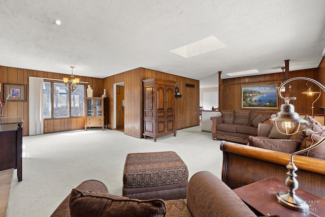 living area featuring a skylight, wood walls, a textured ceiling, light colored carpet, and a chandelier