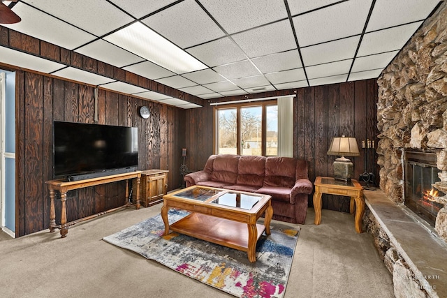 living room with wooden walls, carpet flooring, a fireplace, and a drop ceiling