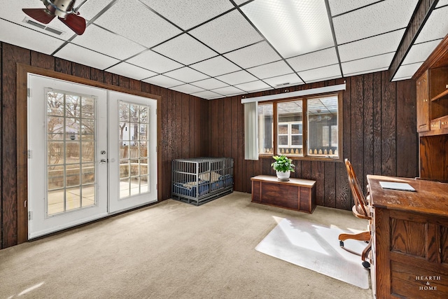 carpeted home office with wooden walls, plenty of natural light, french doors, and visible vents