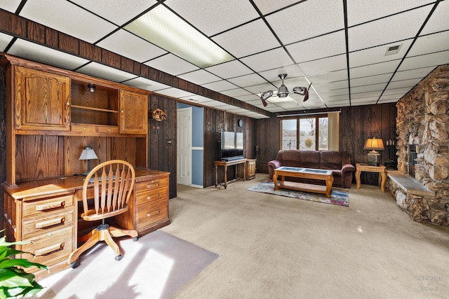 home office featuring visible vents, a drop ceiling, a stone fireplace, built in desk, and wood walls