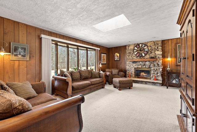 carpeted living area with a skylight, wooden walls, a fireplace, and a textured ceiling