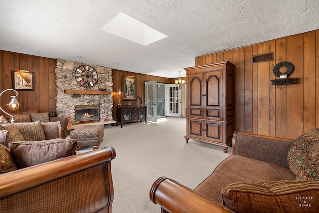 living room with visible vents, light colored carpet, a stone fireplace, a skylight, and a textured ceiling