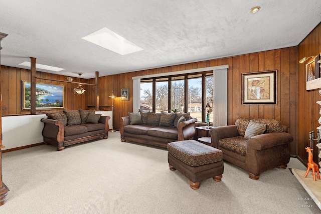 living room featuring wooden walls, baseboards, light carpet, a skylight, and a textured ceiling