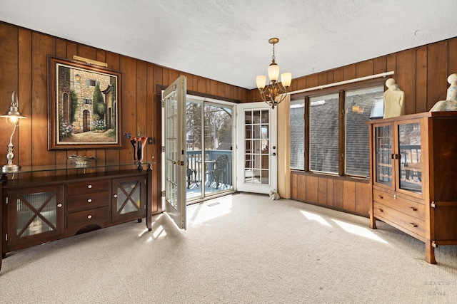 carpeted dining area featuring a textured ceiling, wood walls, and a chandelier